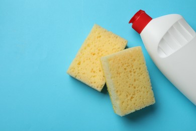 Photo of Sponges and dish soap on light blue background, top view. Space for text