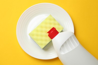 Photo of Sponge, plate and dish soap on yellow background, top view