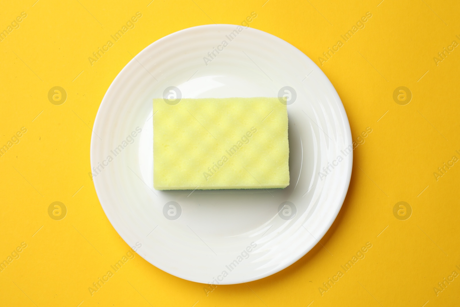 Photo of Plate with sponge on yellow background, top view