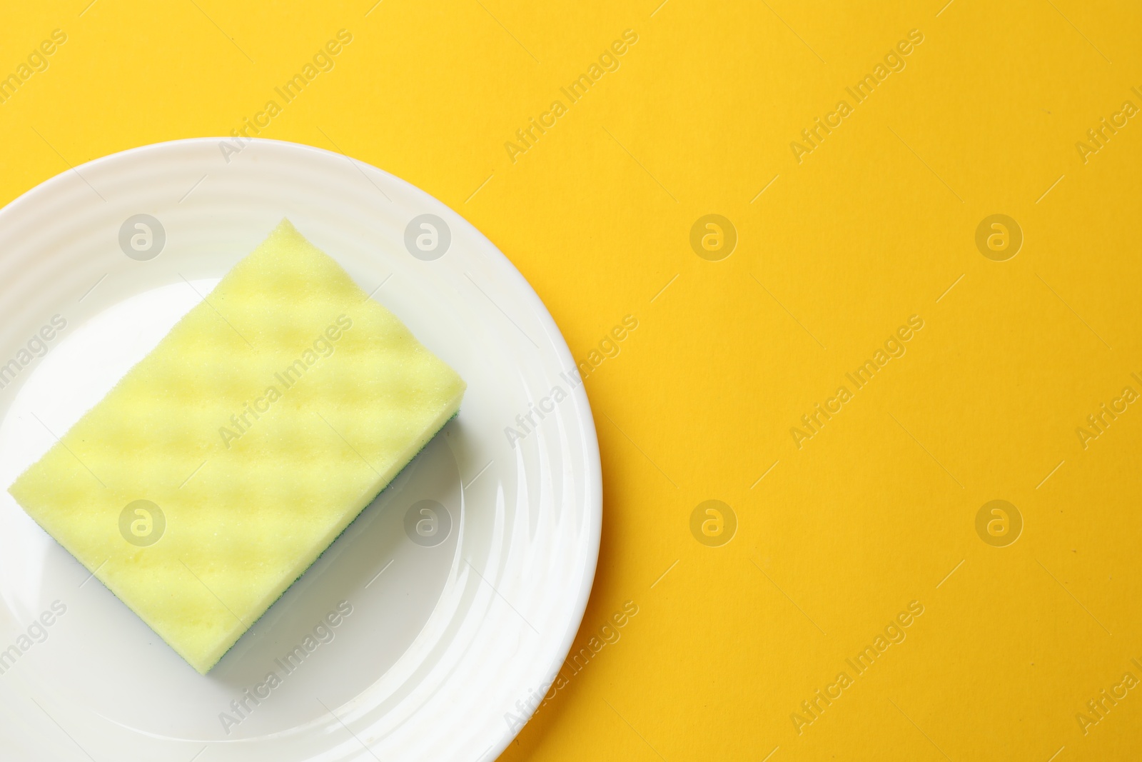 Photo of Plate with sponge on yellow background, top view. Space for text