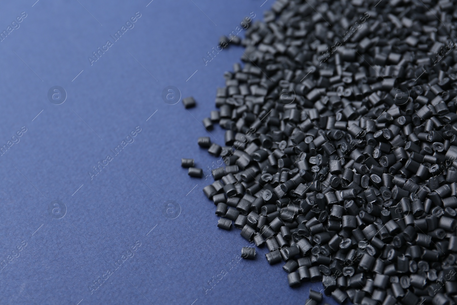 Photo of Pile of black plastic granules on blue background, closeup. Space for text