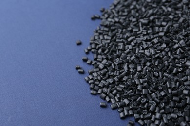 Photo of Pile of black plastic granules on blue background, closeup. Space for text