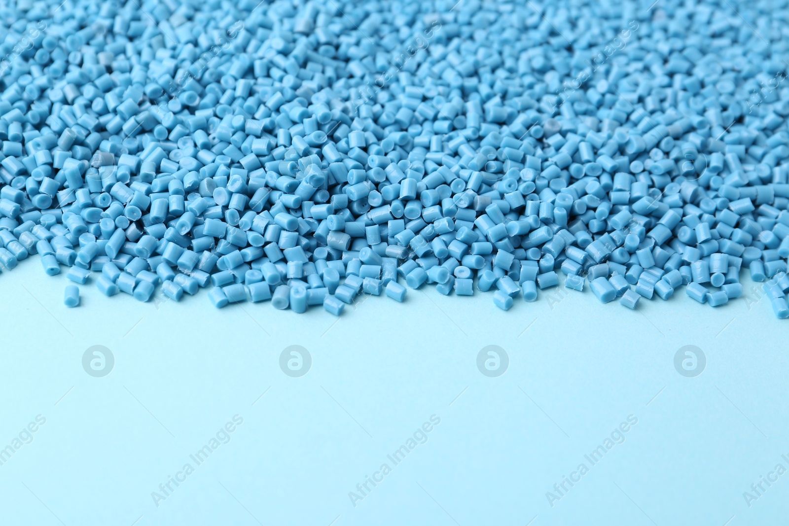 Photo of Pile of plastic granules on light blue background, closeup. Space for text