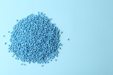 Pile of plastic granules on light blue background, top view. Space for text