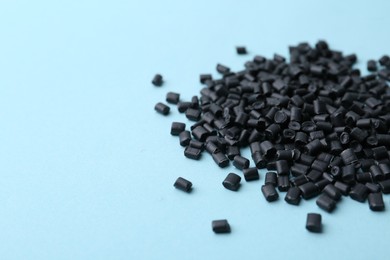 Pile of black plastic granules on light blue background, closeup. Space for text