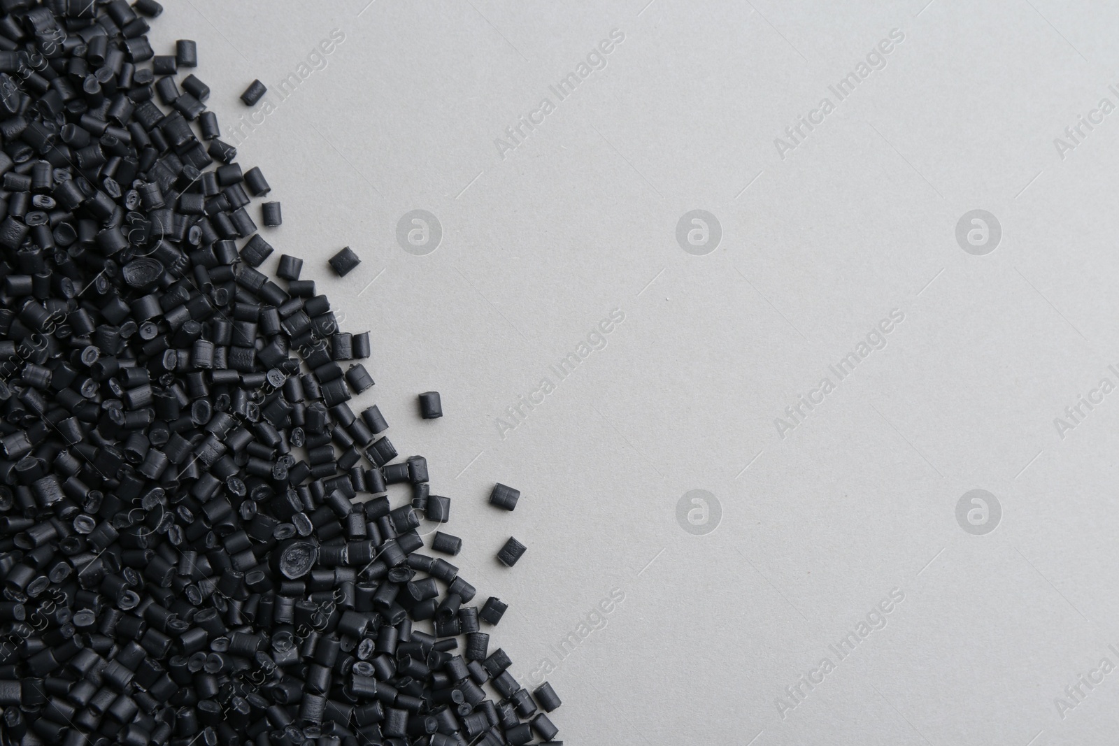 Photo of Pile of black plastic granules on grey background, top view. Space for text