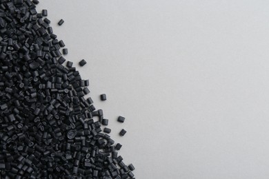 Photo of Pile of black plastic granules on grey background, top view. Space for text