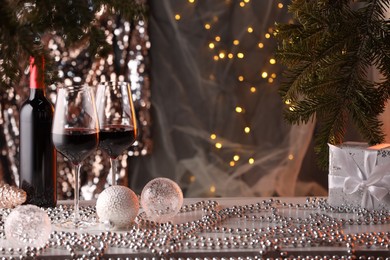 Photo of Red wine and beautiful Christmas decor on white table against blurred lights