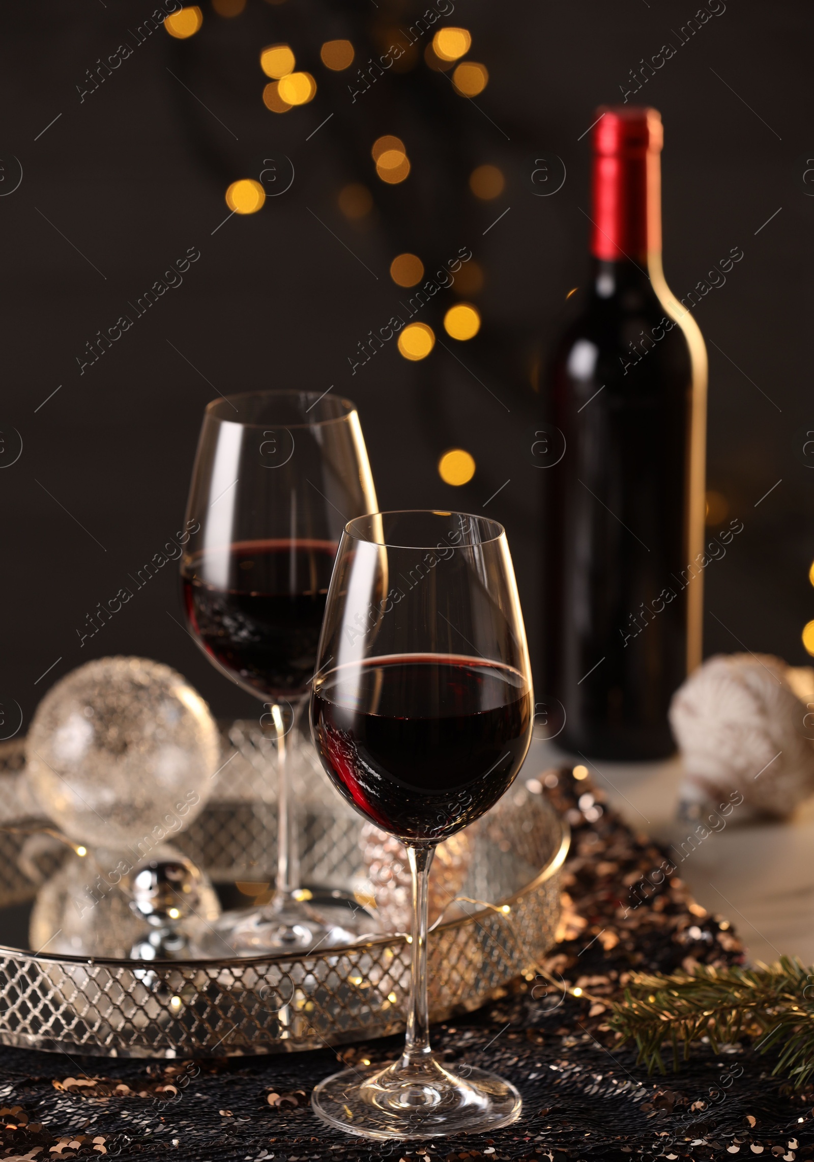 Photo of Red wine and beautiful Christmas decor on table against blurred lights