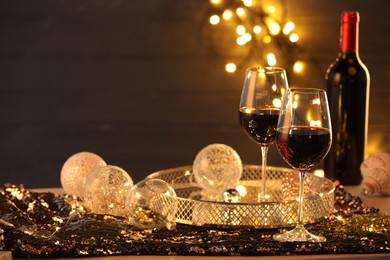 Photo of Red wine and beautiful Christmas decor on table against blurred lights, space for text