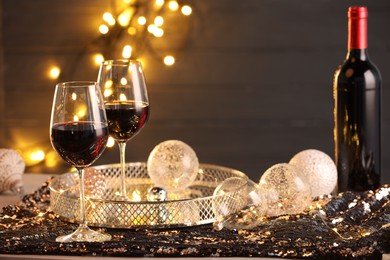 Photo of Red wine and beautiful Christmas decor on table against blurred lights