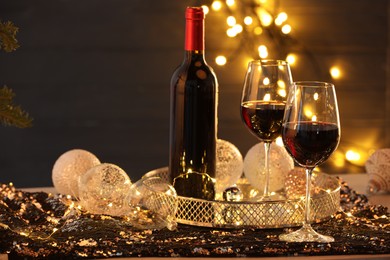 Photo of Red wine and beautiful Christmas decor on table against blurred lights