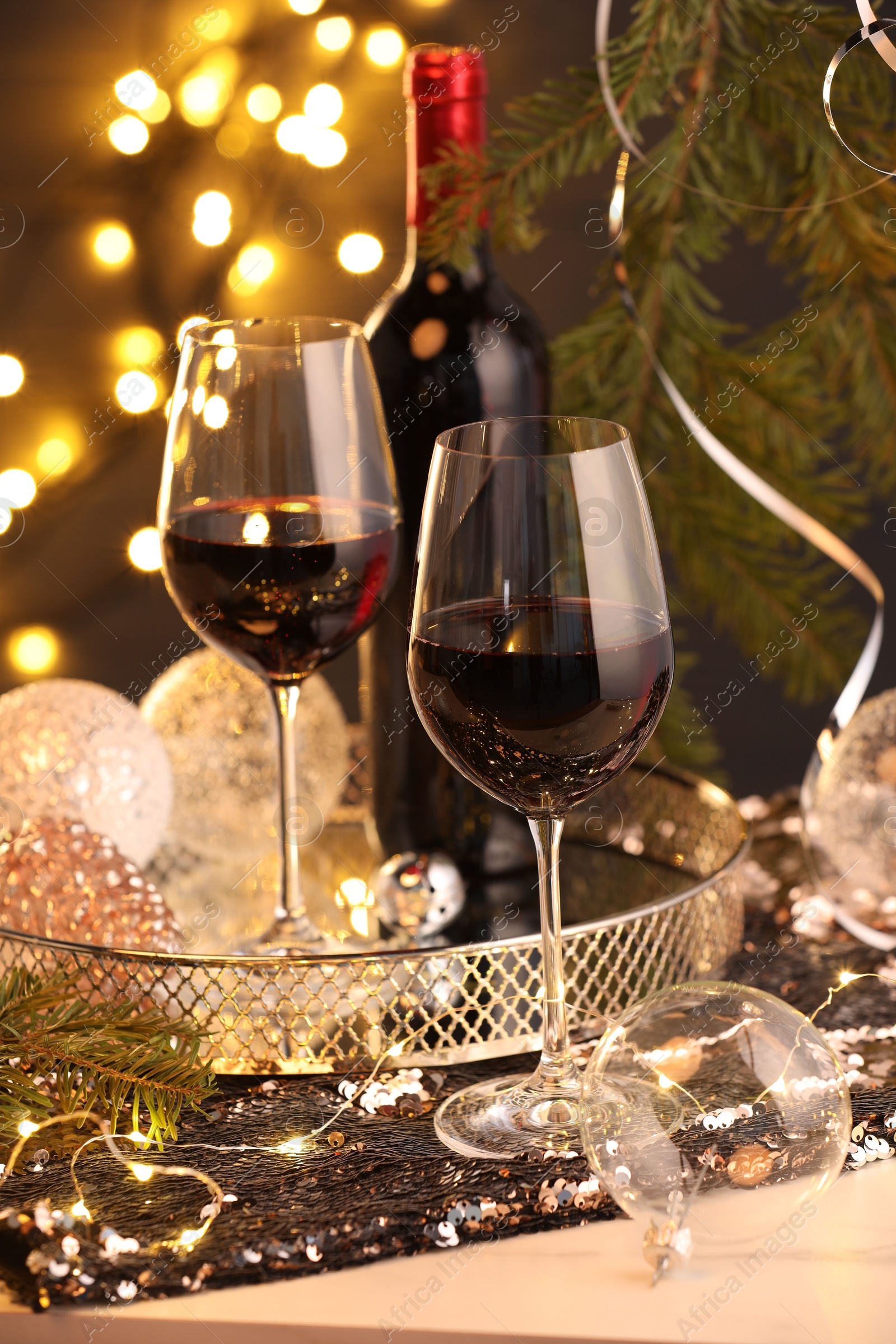 Photo of Red wine and beautiful Christmas decor on white table against blurred lights