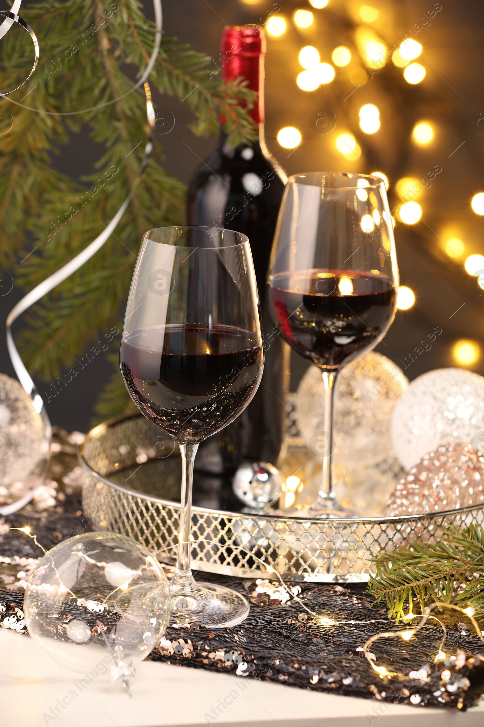 Photo of Red wine and beautiful Christmas decor on white table against blurred lights