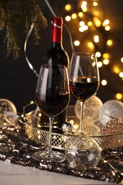 Photo of Red wine and beautiful Christmas decor on white table against blurred lights