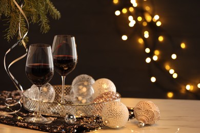 Photo of Glasses with red wine and beautiful Christmas decor on white table against blurred lights, space for text