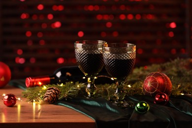 Photo of Glasses with red wine and beautiful Christmas decor on wooden table