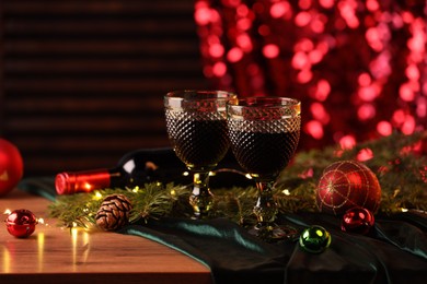 Photo of Glasses with red wine and beautiful Christmas decor on wooden table