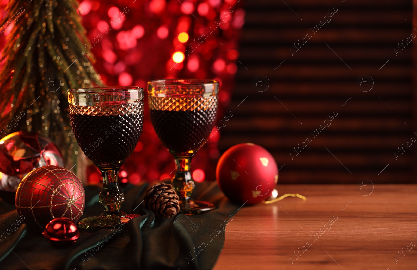 Photo of Glasses with red wine and beautiful Christmas decor on wooden table, closeup. Space for text