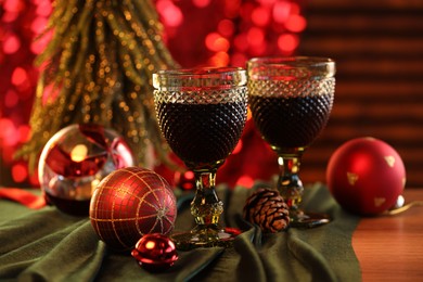 Photo of Glasses with red wine and beautiful Christmas decor on wooden table, closeup