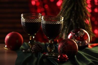 Photo of Glasses with red wine and beautiful Christmas decor on wooden table, closeup