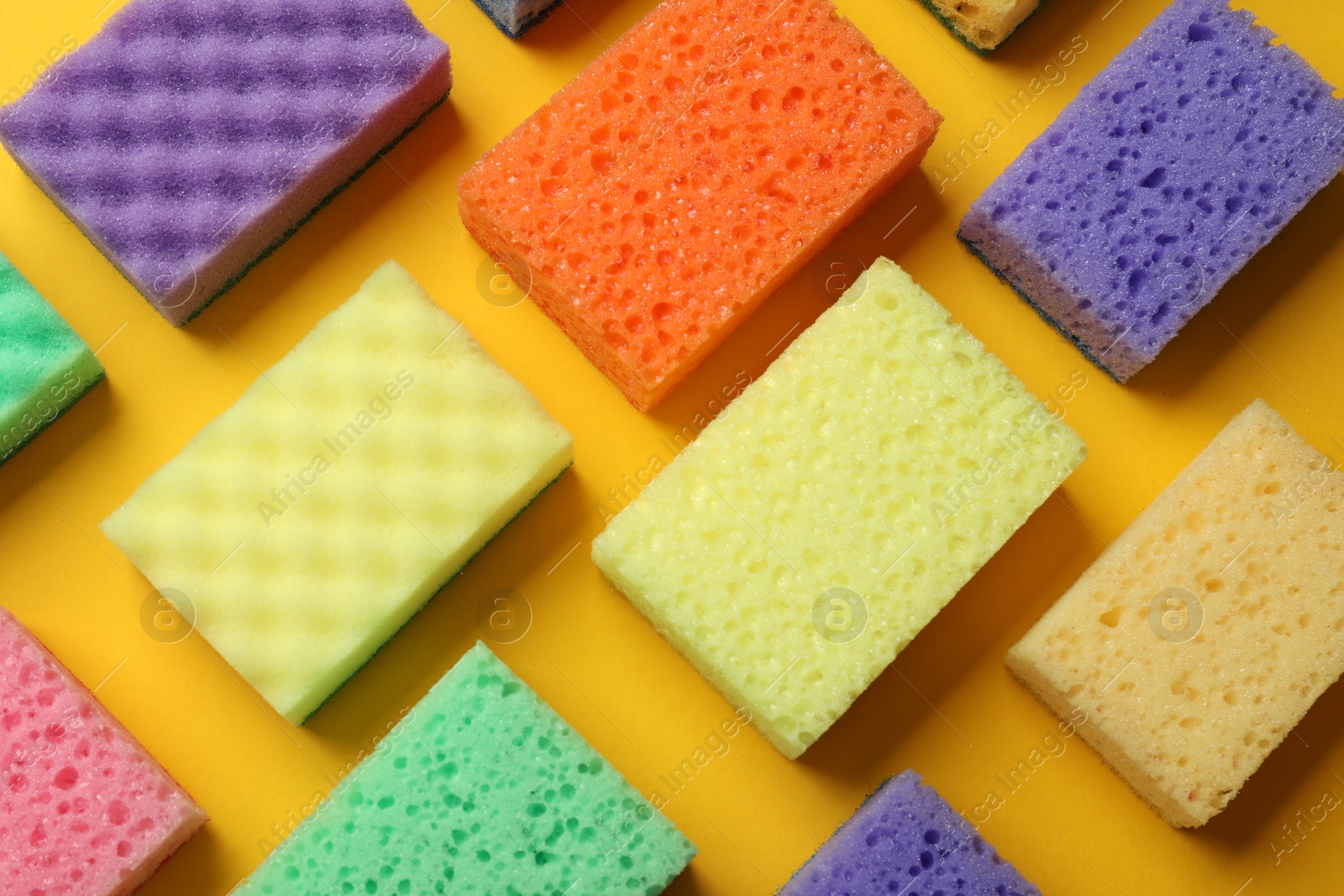 Photo of Colorful sponges on yellow background, flat lay. Cleaning tool