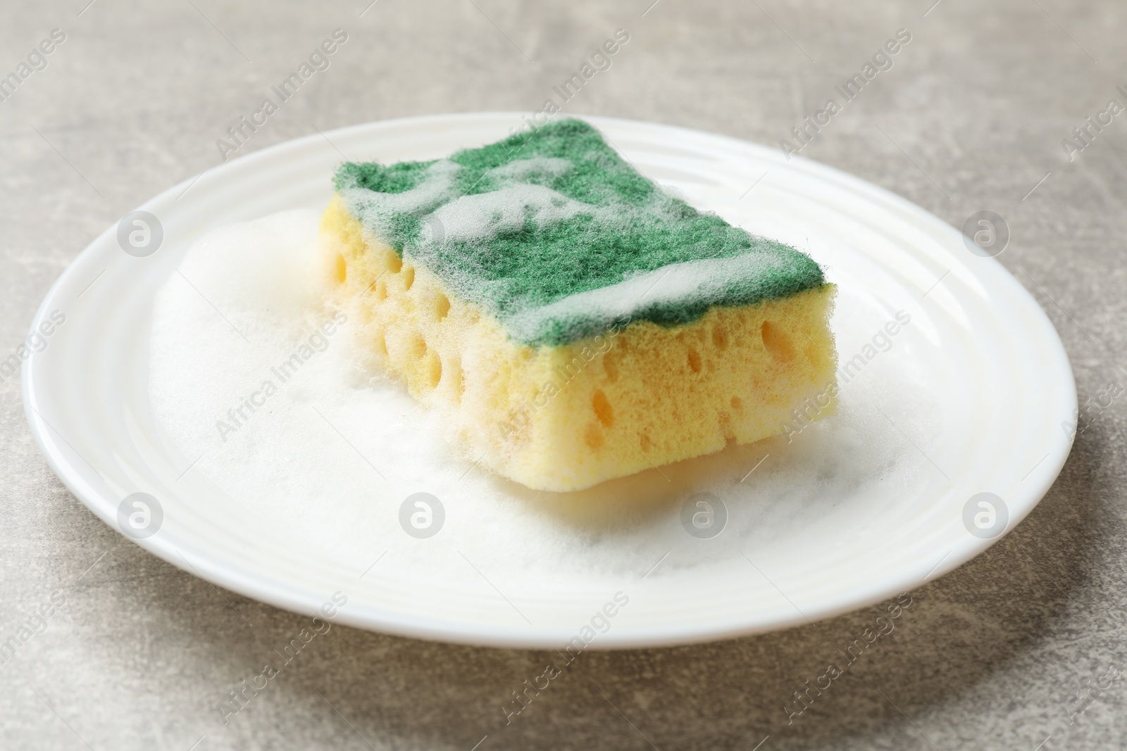 Photo of Soft sponge with foam and plate on gray textured table, closeup