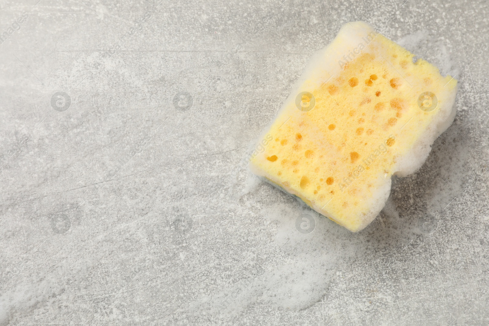 Photo of Yellow sponge with foam on gray textured table, top view. Space for text