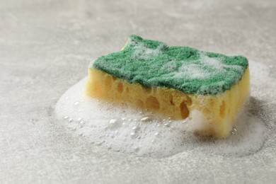 Photo of Soft sponge with foam on gray textured table, closeup. Space for text