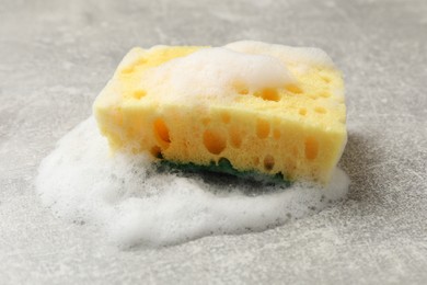 Photo of Yellow sponge with foam on gray textured table, closeup