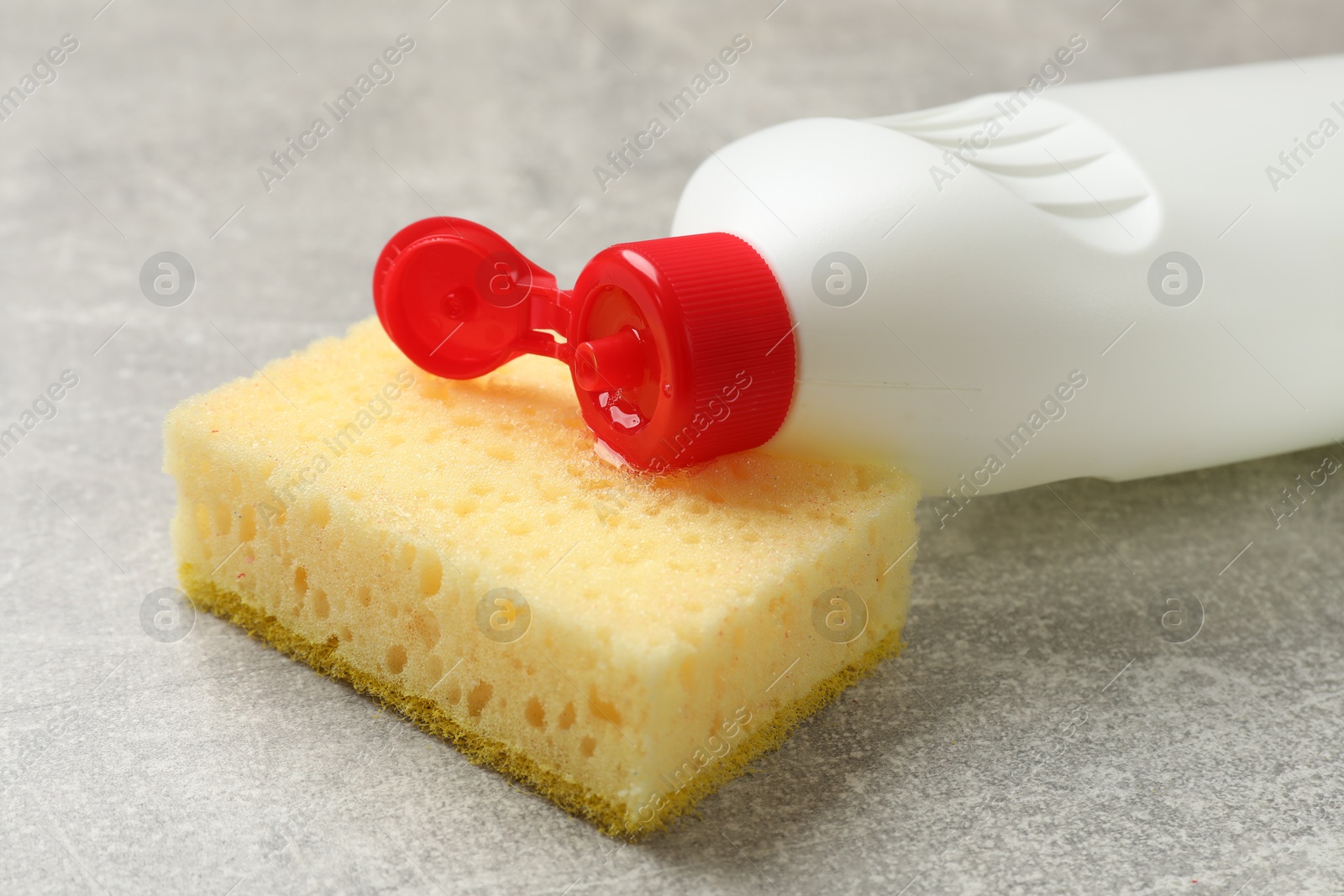 Photo of Yellow sponge and dish soap on gray textured table, closeup