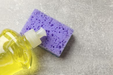 Photo of Violet sponge and dish soap on gray textured table, flat lay. Space for text