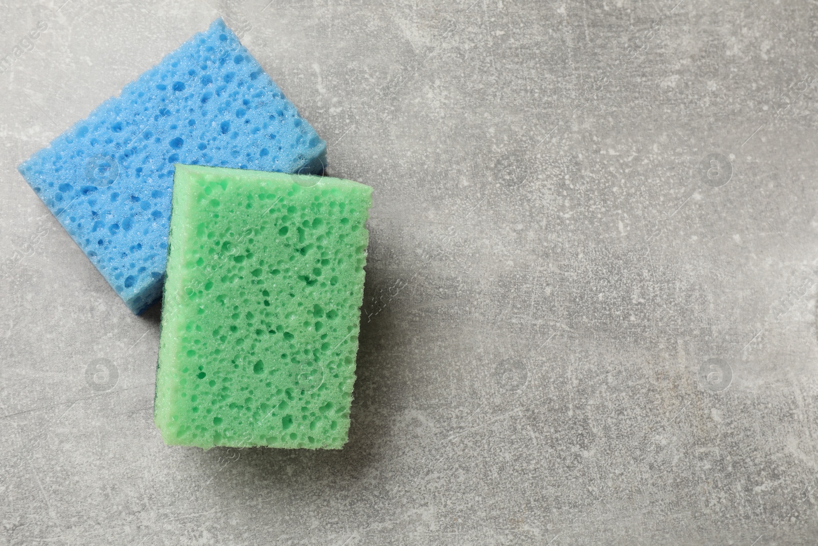 Photo of Soft sponges with foam on gray textured table, top view. Space for text