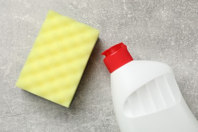 Photo of Yellow sponge and dish soap on gray textured table, flat lay