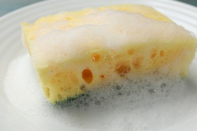 Photo of Yellow sponge with foam on plate, closeup