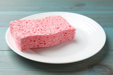 Photo of Pink sponge with foam and plate on light blue wooden table, closeup