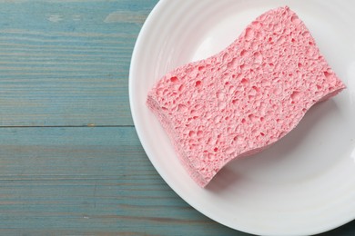 Photo of Pink sponge with foam and plate on light blue wooden table, top view. Space for text