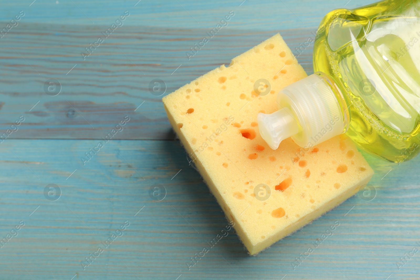 Photo of Yellow sponge and dish soap on light blue wooden table, flat lay. Space for text