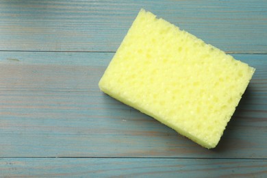 Photo of Yellow sponge on light blue wooden table, top view. Space for text