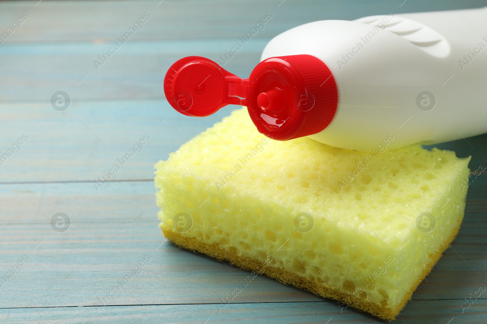 Photo of Yellow sponge and dish soap on light blue wooden table, closeup. Space for text