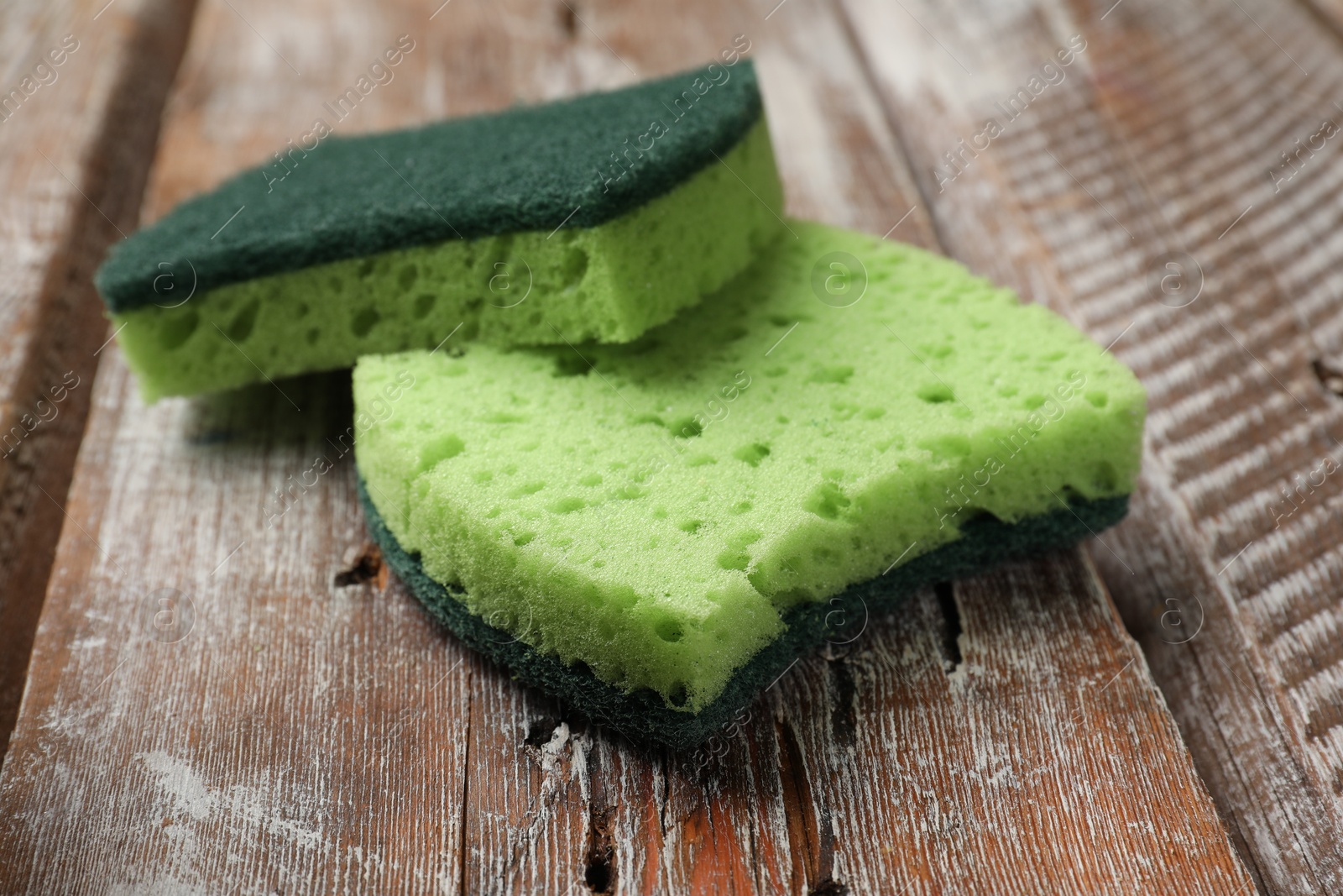 Photo of Two green sponges on wooden table, closeup