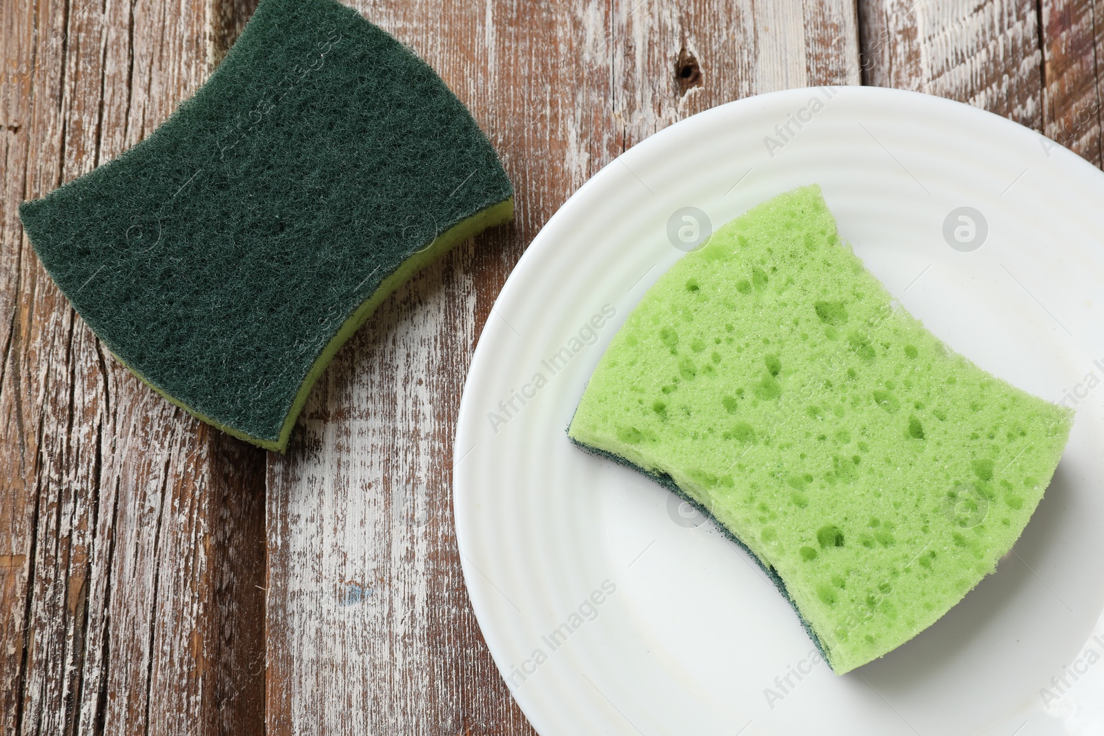 Photo of Green sponges and plate on wooden table, flat lay