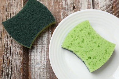 Photo of Green sponges and plate on wooden table, flat lay