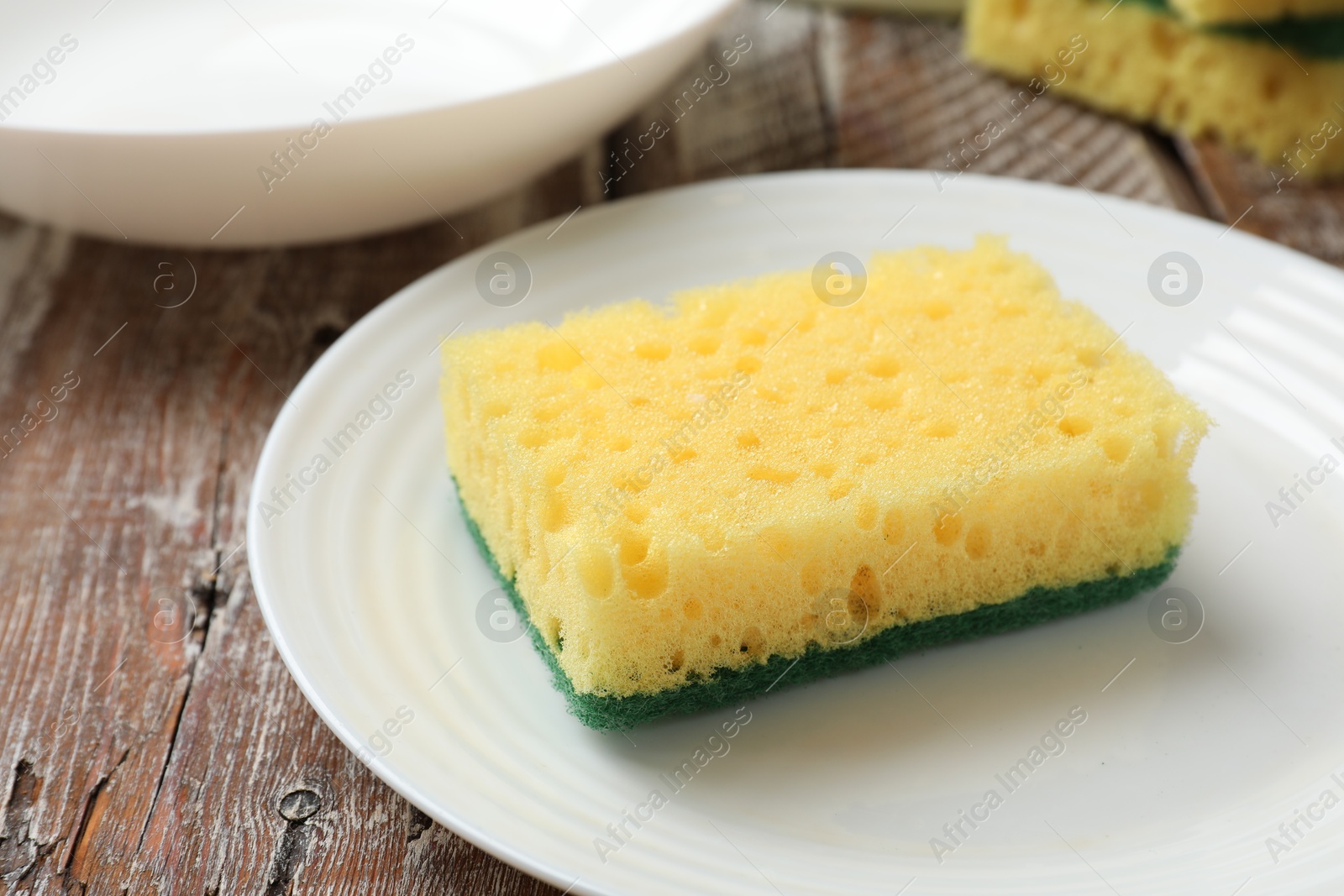 Photo of Yellow sponge, plate and bowl on wooden table, closeup