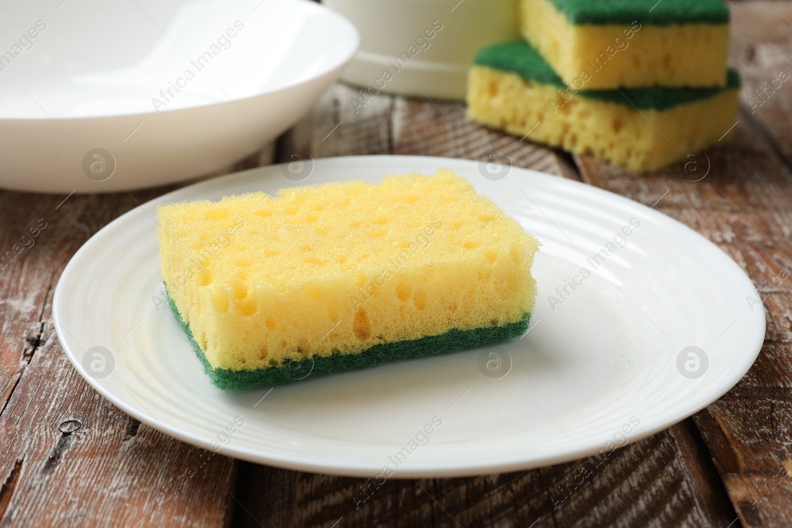 Photo of Yellow sponges and dishware on wooden table, closeup