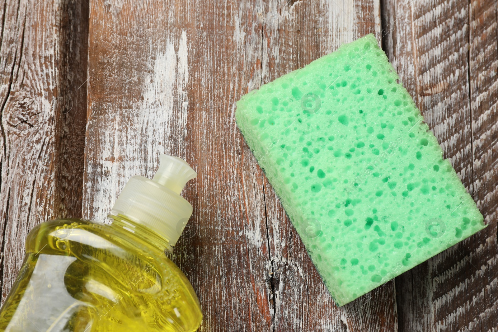 Photo of Green sponge and dish soap on wooden table, flat lay