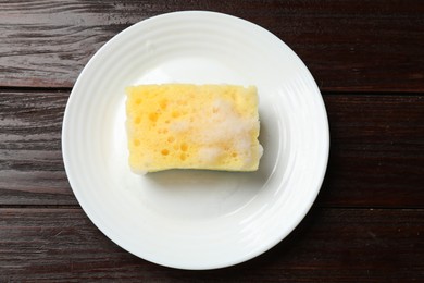 Photo of Yellow sponge with foam and plate on wooden table, top view