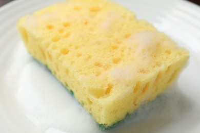 Photo of Yellow sponge with foam on plate, closeup