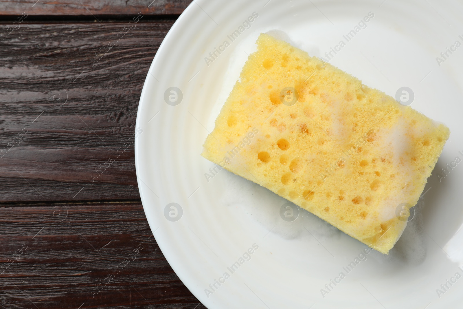 Photo of Yellow sponge with foam and plate on wooden table, top view. Space for text