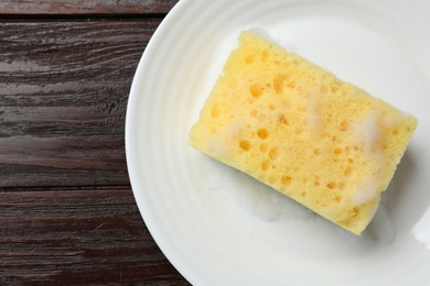 Photo of Yellow sponge with foam and plate on wooden table, top view. Space for text